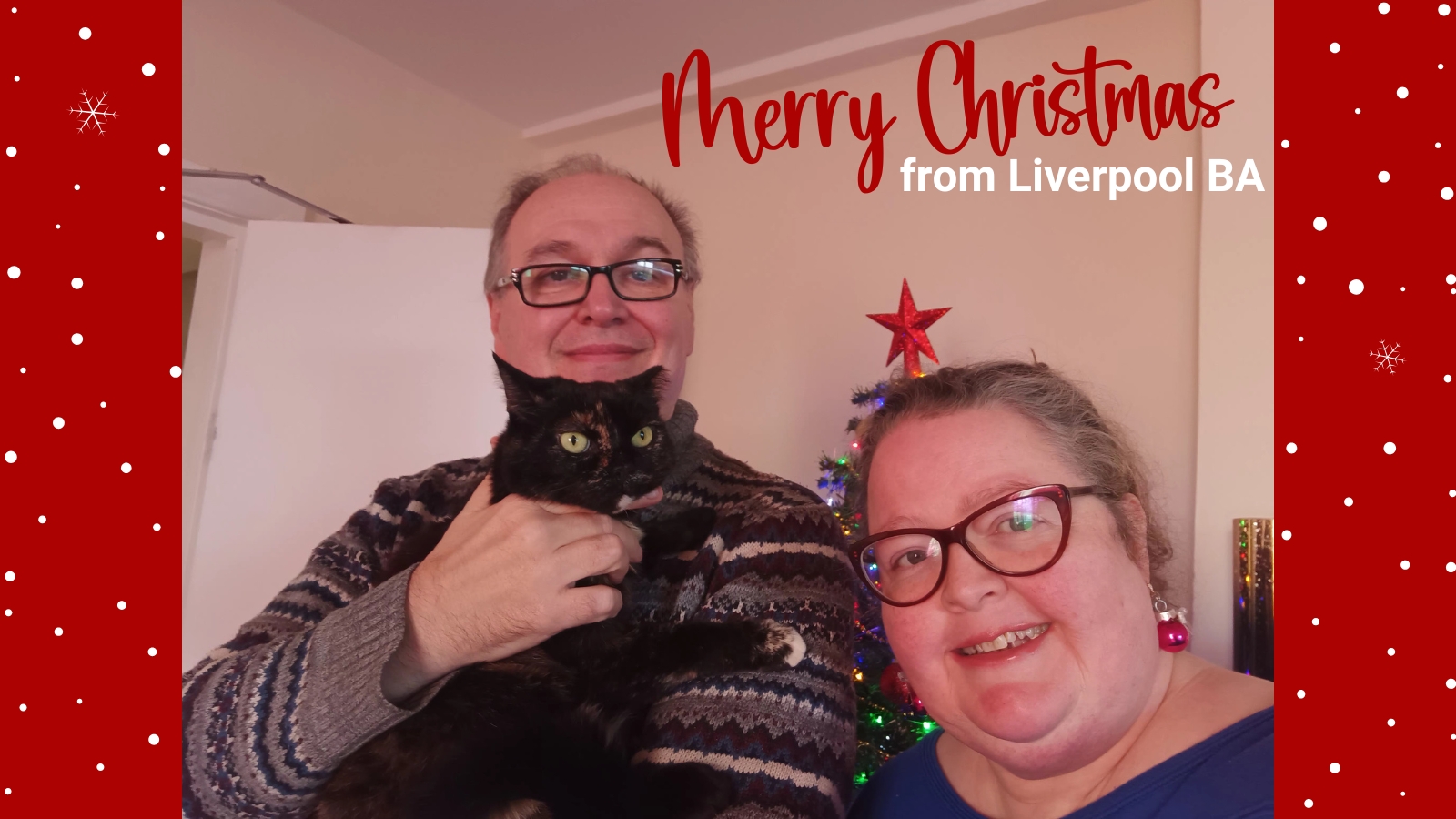 Tony-Kathy-Haines- with-cat-standing-in -front-of-Christmas- tree-text-reads-Merry- Christmas-from-Liverpool-BA